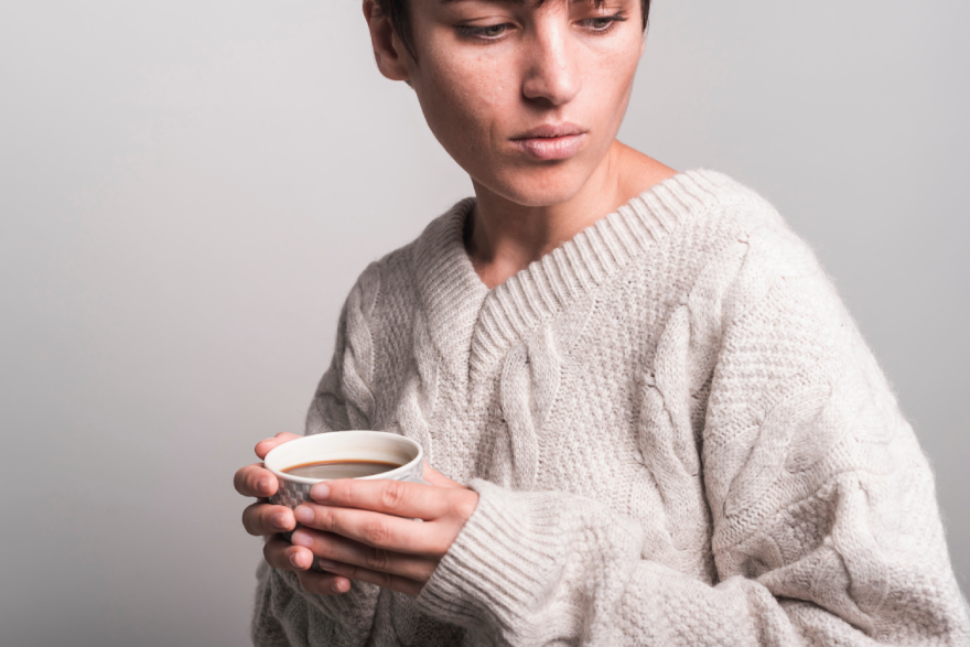 Wegovy vs Mounjaro: a woman holding a cup of coffee, looking ill.